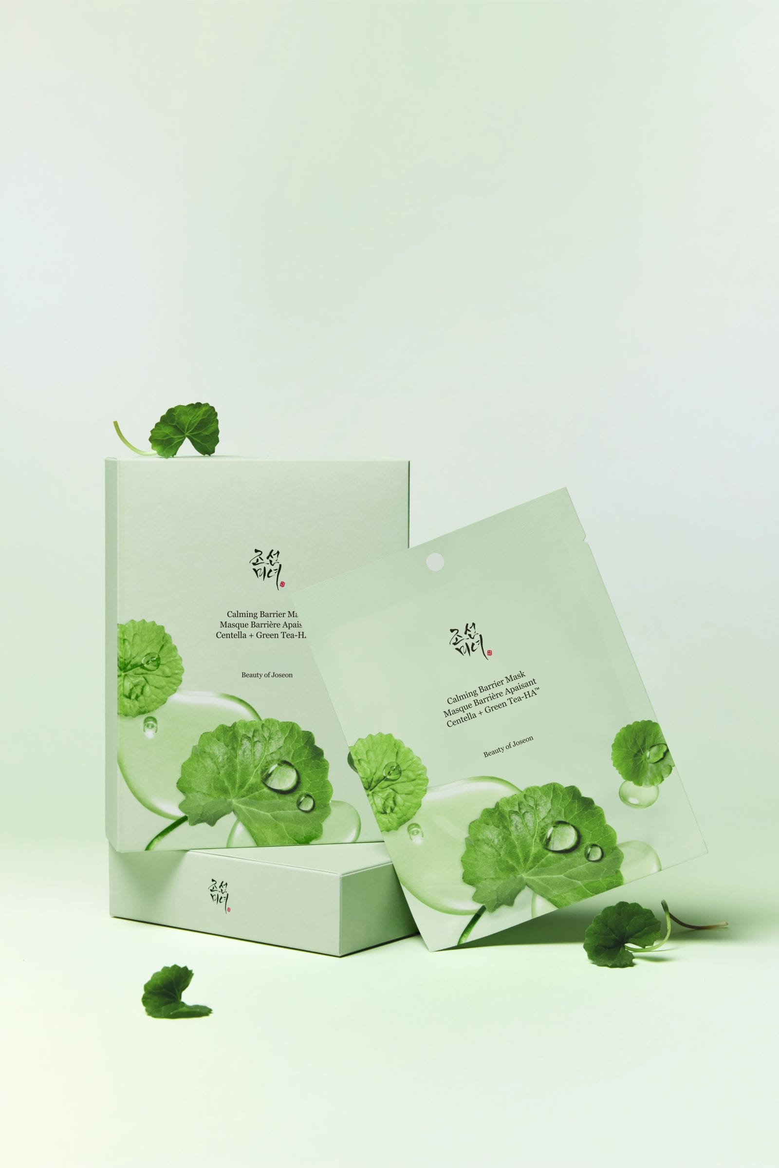 A pale mint green skincare product box and matching sachet package with printed green lotus leaf graphics and small water droplets, arranged on a clean white background with a few loose leaves around them.